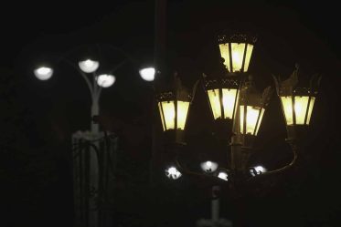 Two different street lanterns on black sky background. Old fashioned and modern street lamps with yellow and white lights in the city street at night.